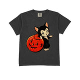A dark gray short-sleeve t-shirt featuring a graphic of a cute black and white kitten holding a carved orange pumpkin, displayed against a solid white background.