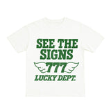White t-shirt with green text 'SEE THE SIGNS 777 LUCKY Dept.' on a white background